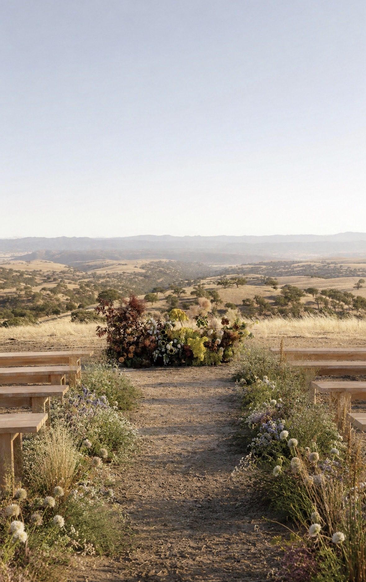 Benches set along a decomposed-granite aisle on the ridge, with a floral installation and the valley beyond